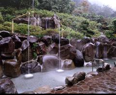A serene outdoor hot spring bath surrounded by natural rock formations, lush greenery, and gentle waterfalls creating a tranquil and inviting atmosphere.