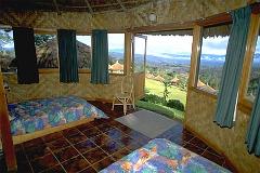 Interior of a thatch-roofed Ambua Lodge room featuring tiled floor, two beds, a chair, and curtains with an open door offering a scenic view of the lush landscape.
