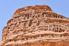 A weathered sandstone rock formation riddled with holes stands against a clear blue sky.