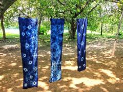 Three blue tie-dye scarves hang on a clothesline strung between trees in a sunny outdoor setting.