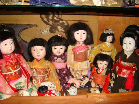 A collection of traditional Japanese Ichimatsu dolls wearing kimonos are displayed on a shelf.