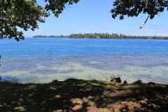 A serene coastal view of Madang, PNG, framed by lush green foliage, showcasing the tranquil blue waters and distant islands under a clear sky.