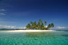 A tropical island paradise featuring crystal-clear turquoise waters, a white sandy beach, and lush palm trees under a bright blue sky.