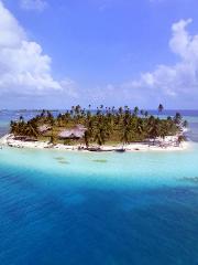 A stunning aerial shot captures a tropical island paradise with turquoise waters, lush palm trees, and charming thatched-roof huts under a partly cloudy sky.