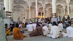 A large gathering of men are seated and standing inside a mosque.