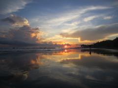 A stunning sunset over a beach, with a person silhouetted on the shore and the sky's colors reflecting in the wet sand.