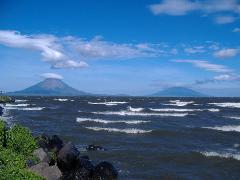 A scenic view of a large body of water with waves, two volcanic islands in the distance, and a blue sky with scattered clouds.