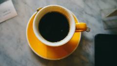 Coffeeholic Tour in Medellin A high-angle shot shows a vibrant yellow cup of black coffee sitting on a matching saucer, positioned on a gray, textured surface.