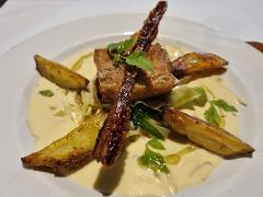 A gourmet dish featuring roasted potatoes and braised meat, garnished with fresh herbs and drizzled with olive oil, served on a creamy sauce.