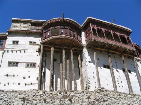 A low-angle shot captures the architectural details of a white building with wooden balconies and supports under a clear blue sky.