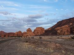 A vast desert landscape with towering rock formations under a cloudy sky, beside a desolate road.