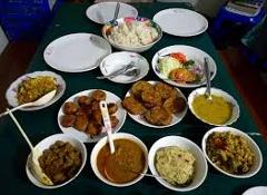 A table is set with a variety of dishes in bowls and on plates, suggesting a shared meal or buffet-style spread.
