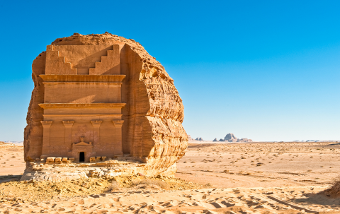 A rock tomb stands in the desert under a clear blue sky.