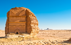 A rock tomb stands in the desert under a clear blue sky.