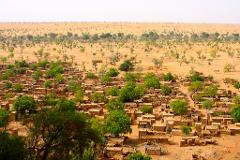 A high-angle shot reveals a dense village nestled within a dry, tree-scattered landscape, showcasing the unique blend of human settlement and nature.