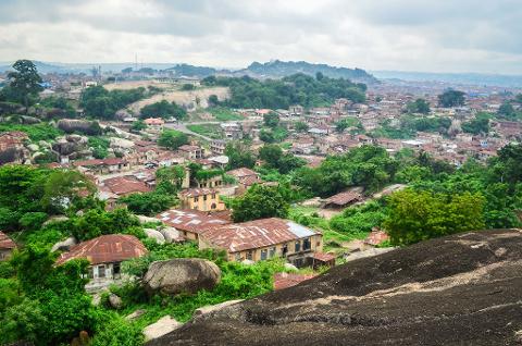 An aerial view showcases a densely populated town nestled amidst lush greenery, rocky outcrops, and buildings with weathered roofs under an overcast sky.