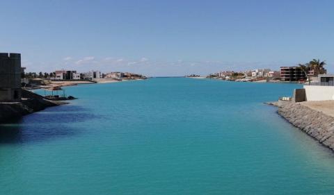 A wide shot of turquoise water between two sides with buildings under a clear blue sky.