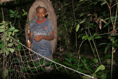 A man in a Carlsberg shirt wears a woven structure on his head while standing in a jungle setting.