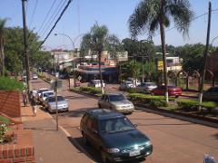 A street view shows parked cars, people walking on the sidewalk, and palm trees under a clear blue sky.