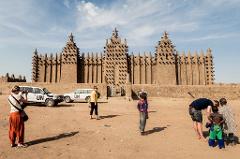 Tourists stand in front of the Great Mosque of Djenné, a large mud brick building, in Mali.