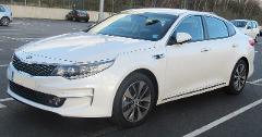 A white Kia Optima parked in a parking lot with other cars in the background.
