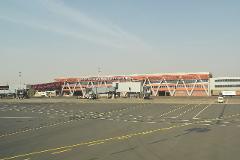 An airport building with the words "AEROPORT INTERNATIONAL PRESIDENT MODIBO KEITA-SENOU" on top of it, connected to jet bridges in an outdoor airport apron.
