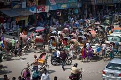5-Day Dhaka Cultural Heritage Tour: Floating Markets & River Life Experience A bustling street scene in Dhaka, Bangladesh, filled with rickshaws, pedestrians, and vendors under a bright, sunny sky.