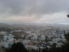 An aerial view of a city nestled amongst rolling hills under a cloudy, overcast sky.