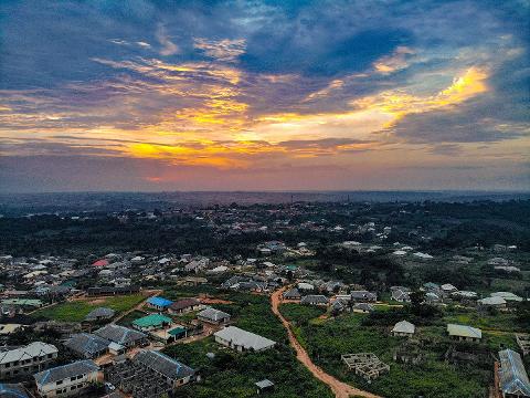 An aerial view captures a town nestled amidst lush greenery under a vibrant sunset sky.