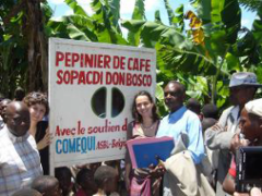 A group of people stand in front of a sign that reads "PEPINIER DE CAFE SOPACDI DON BOSCO" with "COMEQUI ASBL-Belgique" at the bottom, likely promoting a coffee nursery project.