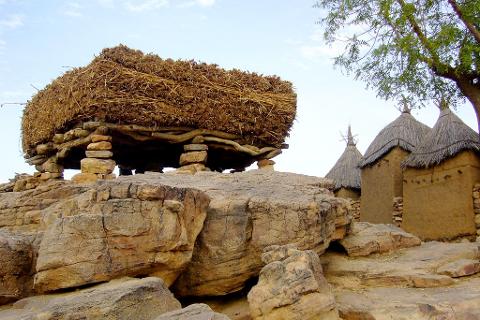 A Dogon village granary on a rock formation with mud buildings with straw roofs in the background, Mali.