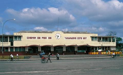 The image shows the Tamatave railway station (Chemin de Fer de Tamatave Cote Est) with people moving about in front of it.