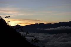 Aventura de observación de aves en Cuchilla San Lorenzo desde Santa Marta A breathtaking view of silhouetted mountains and palm trees against a stunning sunset with clouds filling the valley below.