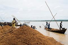Men in boats are collecting sand from a river, forming a large pile near the shore.