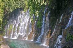 A beautiful waterfall cascades down a lush, green cliff into a clear, serene pool, creating a tranquil and picturesque scene.