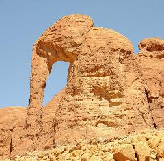 This image depicts a large, reddish-brown rock formation resembling an elephant with a clear blue sky in the background.