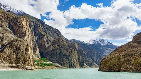 Majestic mountains rise above a serene lake under a partly cloudy sky, creating a breathtaking landscape.