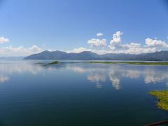 A scenic view of a tranquil lake reflecting the sky and clouds, with mountains in the background and vegetation along the shoreline.