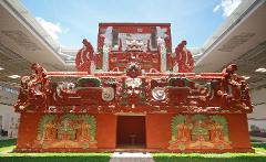 A restored Mayan temple, painted in red with white and green accents, stands under a modern shelter, showcasing the blend of ancient and contemporary architecture.