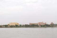 Distant buildings and trees line the horizon across a wide, murky river under a dull sky, creating a tranquil yet hazy cityscape.