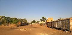 An old, deserted railway yard with dilapidated wagons on either side of a dirt road under a clear blue sky.