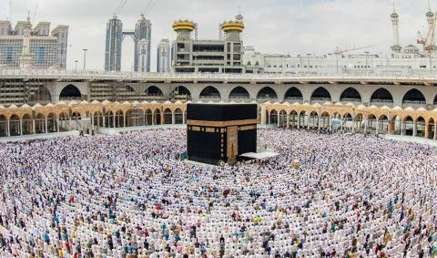 A vast crowd of pilgrims pray around the Kaaba in Mecca, surrounded by the Grand Mosque's architecture.