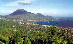 A scenic view of Rabaul, Papua New Guinea, with a volcano in the background, lush vegetation, and a bay dotted with boats.
