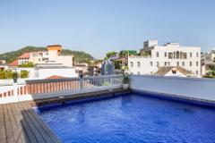 Panama City and San Blas Here's a description of the image:A rooftop pool with blue tiles is surrounded by a deck and railing, overlooking a neighborhood of white buildings and a hill in the background on a sunny day.