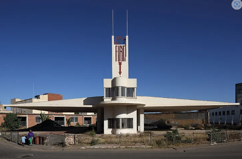 An old Fiat car dealership with an art deco style design under a blue sky, with a sign and architectural elements representing the car brand.