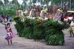 The image shows a vibrant cultural scene, with people in elaborate grass costumes and masks performing a traditional dance or ceremony in Papua New Guinea.