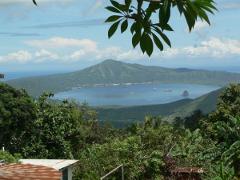 A scenic view of Rabaul's harbor and surrounding volcanic landscape, framed by lush green trees.