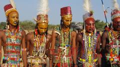 A group of men in traditional attire and face paint stand together, likely as part of a cultural performance or celebration.