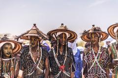 A group of men in traditional clothing and face paint stand in a line, showcasing the culture and artistry of the people participating in the Bianou & Gerewol Festival.