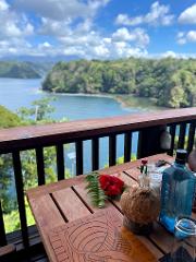 A refreshing coconut drink with a red hibiscus flower sits on a wooden table overlooking a scenic bay at Tufi Resort.